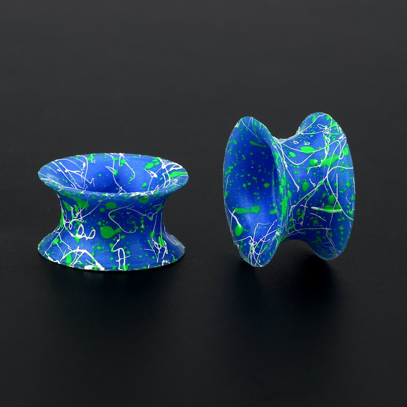 May include: Two blue and green ear gauges with a white splatter paint design. The gauges are made of a smooth, flexible material.