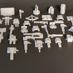 May include: A collection of 3D printed miniature models of various weapons and accessories, including cannons, turrets, and barrels. The models are all gray and appear to be made of plastic.