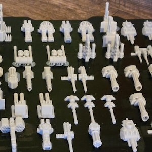 May include: A collection of 3D printed white plastic miniature models of various shapes and sizes. The models are arranged on a black surface with the text "Bamboo Smooth PEI Plate" visible in the background.