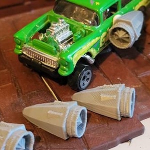 May include: A green toy car with a detailed engine and five gray plastic rocket boosters. The car is sitting on a brown wooden surface.