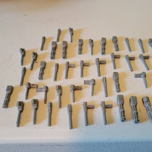 May include: A collection of 40 gray plastic miniature guns, some with multiple barrels, arranged in rows on a white surface.
