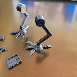May include: A set of 3D printed model pieces for a sci-fi robot. The set includes two robot arms with articulated joints, a rectangular base, and two sets of three barrels.