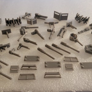 May include: A collection of gray plastic model parts for a ship or other vehicle. The parts include guns, turrets, and other details.