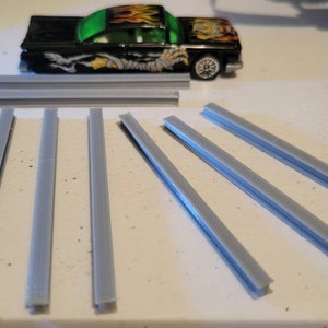May include: Eight gray plastic track pieces for a toy car race track.