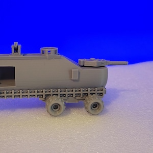 May include: A gray model of a military vehicle with a tank-like structure and a trailer. The model has a detailed design, including wheels, a cannon, and a hatch. The vehicle is set against a blue background.