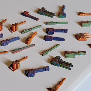 May include: A collection of 20 miniature 3D printed guns in various colors, including orange, blue, and green. The guns are made of plastic and have a detailed design.