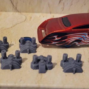 May include: Eight gray plastic toy car parts with a red toy car with an American flag design in the background.
