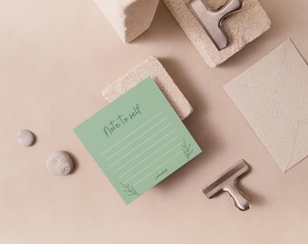 May include: A green notepad with the text "Note to self" written in black ink. The notepad has lined paper and a small floral design in the bottom right corner.