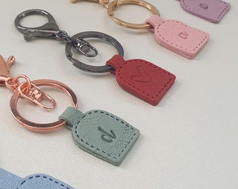 May include: Five leather keyrings with different coloured leather and metal rings. The keyrings have different coloured leather tags with the letter "d" embossed on them. The colours are purple, pink, red, green, and blue.
