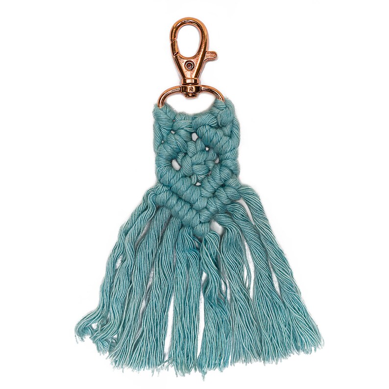 May include: A teal blue macrame keychain with a copper-colored metal clasp. The keychain has a fringe of tassels.