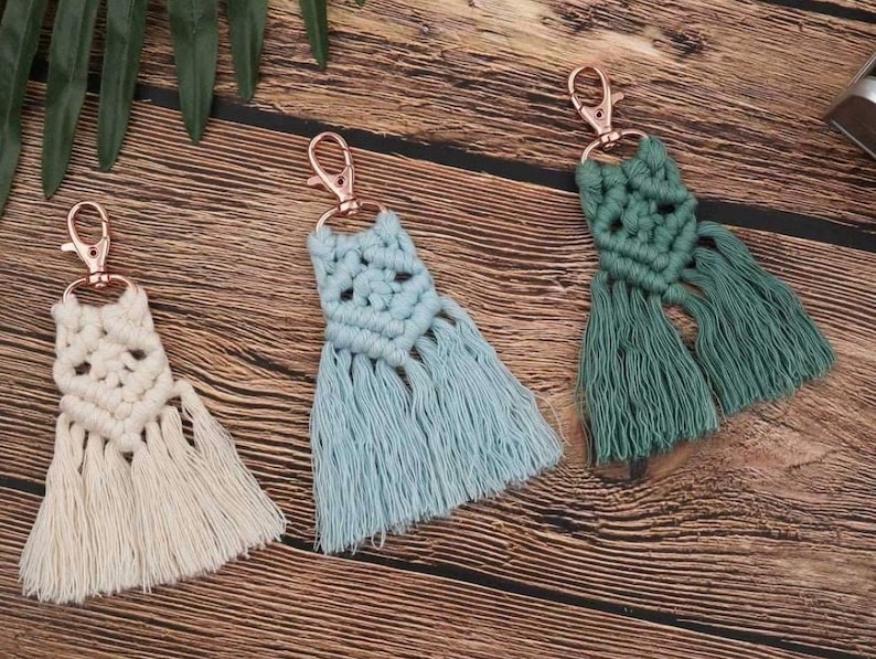 May include: Three handmade macrame keychains with tassels. The keychains are in beige, light blue, and green.