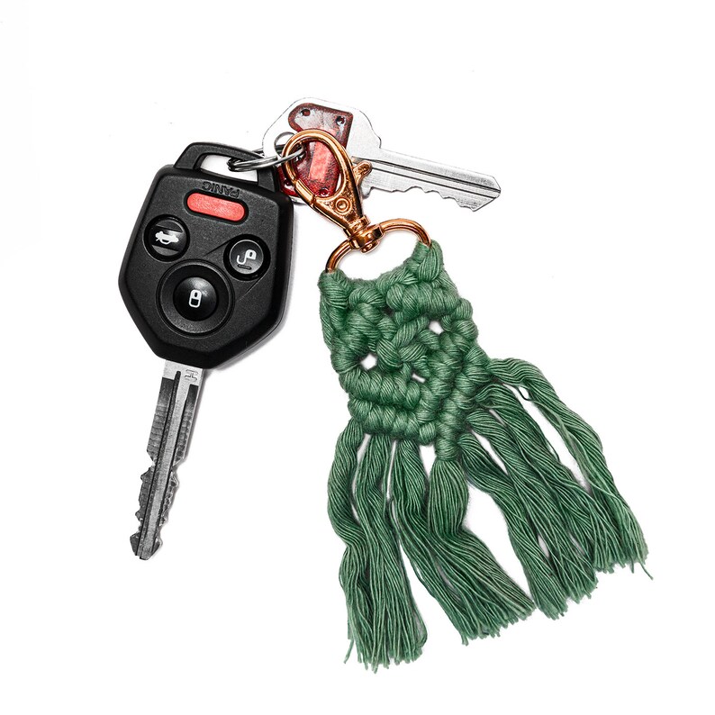 May include: A green macrame keychain with a tassel attached to a silver key and a black car key fob. The keychain has a gold metal ring.