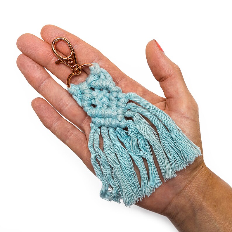 May include: A light blue macrame keychain with a gold-colored metal clasp and a fringe tassel.