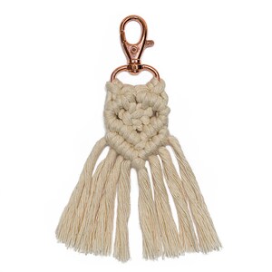 May include: A white macrame keychain with a rose gold metal clasp and a fringe tassel.