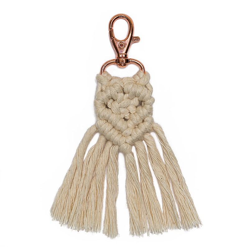May include: A white macrame keychain with a rose gold metal clasp and a fringe tassel.