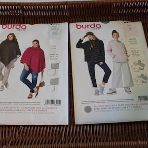 May include: Two Burda Style sewing pattern magazines featuring images of women wearing capes, hoodies, and pants. The magazines are on a woven wicker tray. The text on the magazines includes "Burda Style" and "All patterns with seam and hem allowances."