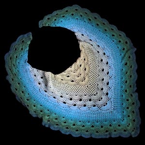 May include: A crocheted shawl with a gradient of green, blue, and white colors. The shawl is made with a delicate stitch pattern and has a scalloped edge.