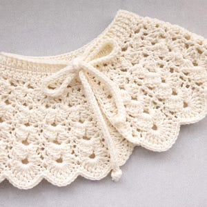 Peut inclure: Col de chemise en crochet crème, avec un bord festonné et une fermeture à nouer délicate. Le col fait à la main présente un motif ajouré, mettant en valeur le travail de couture complexe. Cet accessoire ajoute une touche de charme vintage à n'importe quelle tenue.
