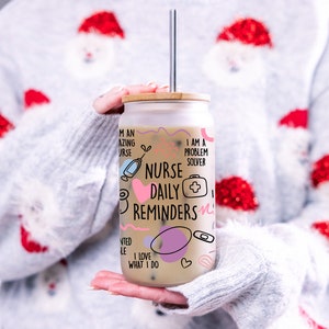 May include: A white glass tumbler with a bamboo lid and a straw. The tumbler has a pink and black design with the text "Nurse Daily Reminders" and other related phrases.