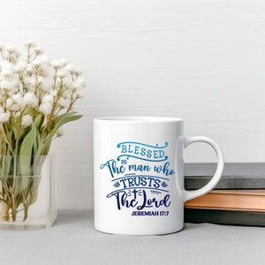 May include: White ceramic mug with a blue and white gradient design. The mug features the text "Blessed is the man who trusts the Lord" with a cross symbol and the scripture reference "Jeremiah 17:7".