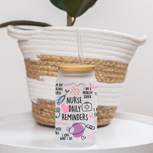 May include: White glass water bottle with a bamboo lid and a straw. The bottle has a pink and purple design with the text "Nurse Daily Reminders" and other related phrases.