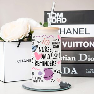 May include: White stainless steel tumbler with a pink, blue, and purple design. The tumbler has a bamboo lid and a straw. The design includes the words "Nurse Daily Reminders" and "I am a problem solver".