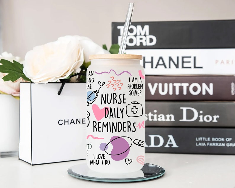 May include: White stainless steel tumbler with a pink, blue, and purple design. The tumbler has a bamboo lid and a straw. The design includes the words "Nurse Daily Reminders" and "I am a problem solver".