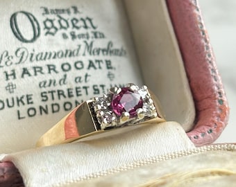 Pode incluir: Um anel de ouro com uma pedra preciosa rosa redonda central, rodeada por pedras brancas menores. O anel é definido em um design quadrado. O anel está dentro de uma caixa de joias rosa com o texto "James R Ogden & Sons Ltd, Diamond Merchants, Harrogate and at Duke Street St, London."