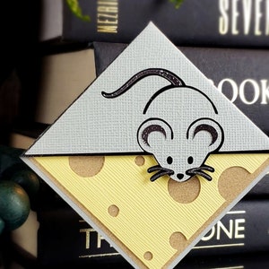 May include: A gray and white mouse bookmark with a cheese design. The mouse is holding a piece of cheese with holes in it.