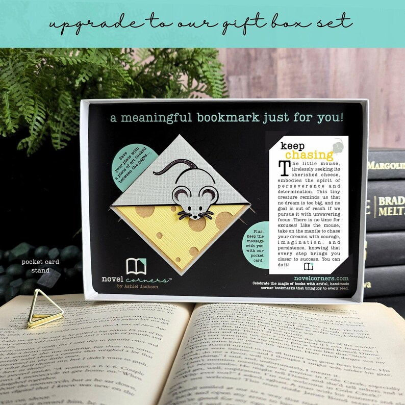Może przedstawiać: Biało-ż&oacute;łta zakładka narożna w kształcie myszy na kawałku sera, prezentowana w czarnym pudełku upominkowym z napisem a meaningful bookmark just for you oraz keep chasing, obok małego złotego tr&oacute;jkątnego stojaka na karty.