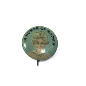 May include: A vintage button with a blue and white design. It features a portrait of a woman with the text "In Honor of Mother" around the edge.