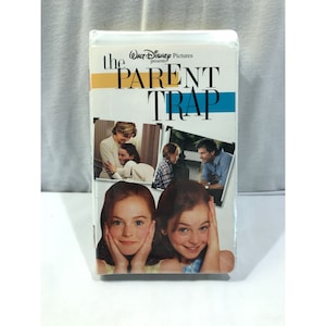 Puede incluir: Cinta de VHS sellada de la película de Disney "Juego de Gemelas". La portada presenta el título de la película en letras grandes y en negrita con un diseño de rayas amarillas y azules. También se muestran imágenes del elenco en la portada.