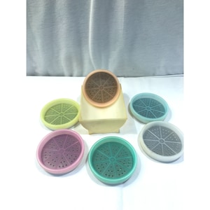 Puede incluir: Un vaporizador de alimentos vintage de color blanquecino con tapa marrón y seis bandejas perforadas de colores en tonos verdes, rosas, azules y grises. El vaporizador tiene una base redondeada y una parte superior rectangular.