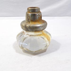 Pode incluir: Um tinteiro de vidro transparente vintage com uma base decorativa canelada e uma parte superior de metal manchado. O tinteiro tem formato bulboso e uma pequena abertura no topo. O metal mostra sinais de idade e desgaste.