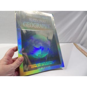 May include: A National Geographic magazine with a holographic cover. The magazine features the title "National Geographic" in large letters. The cover also includes the text "Can Man Save This Fragile Earth?"