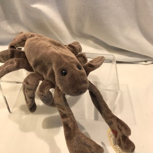May include: A brown plush lobster toy with black eyes and long, articulated claws. The stuffed animal is made of soft, velvety material and has a tag attached. The toy is designed to resemble a lobster.