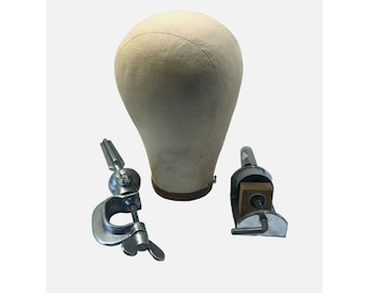 May include: A beige canvas wig head with a dark brown base, flanked by two metal clamps. One clamp is C-shaped with a wingnut, the other has a wooden block. The items are set against a white backdrop.