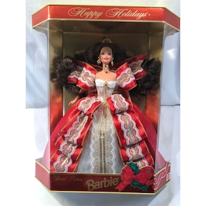 May include: A red and white Barbie doll in a festive holiday dress with gold trim and a large red bow. The doll is in a clear plastic box with a red and gold border. The box says "Happy Holidays" and "Special Edition Barbie".