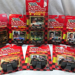 May include: Collection of 1997 Racing Champions NASCAR die-cast cars in their original packaging. The cards are red with a checkered flag design and feature images of the drivers and cars.