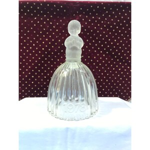 Puede incluir: Una botella decorativa de vidrio transparente con una figura de niño de vidrio esmerilado con las manos juntas en oración. La botella tiene un diseño acanalado en forma de campana y el año "1978" está grabado en la parte delantera.