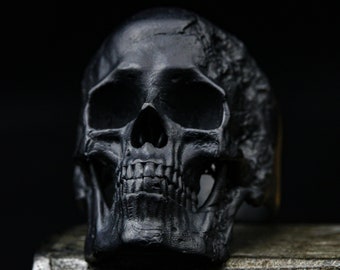 May include: A black skull ring with intricate details. The skull is made of a smooth, matte black material and has a realistic appearance.