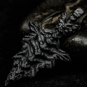 May include: A black, intricately detailed pendant shaped like a jagged, abstract form. The pendant has a rough, textured surface and appears to be made of metal.