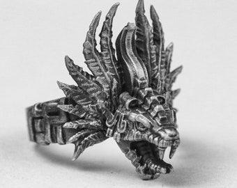 May include: A silver ring with a detailed design of a feathered serpent head. The serpent's mouth is open, revealing sharp teeth. The ring is a statement piece with intricate details.