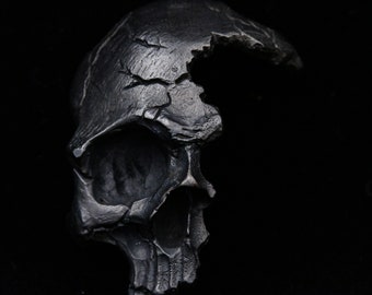 May include: A black metal skull sculpture with a large crack on the side, revealing the inside of the skull.