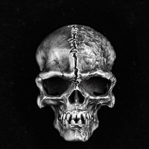 May include: A silver skull sculpture with a detailed, textured surface. The skull has a stitched seam down the center of the head.