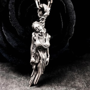 Könnte beinhalten: Eine silberne Halskette mit einem Anhänger, der eine detaillierte Skulptur einer Frau in einem fließenden Kleid zeigt. Der Anhänger hängt an einer silbernen Kette.