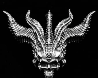 May include: A silver skull with three sets of horns, each horn is detailed with a series of ridges. The skull has a detailed design with a pointed chin and a prominent brow.