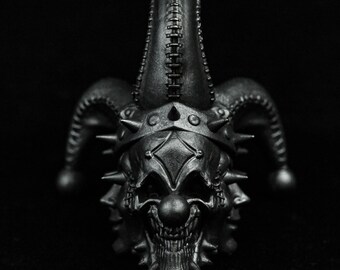 May include: A black metal sculpture of a jester with a skull-like face and a pointed hat. The sculpture has a detailed design with spikes and stitching.