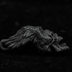 May include: A black metal skull with wings, the skull is lying on its side with the wings spread out.