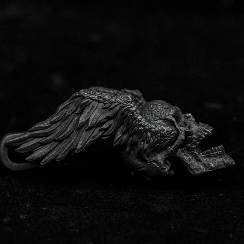 May include: A black metal skull with wings, the skull is lying on its side with the wings spread out.